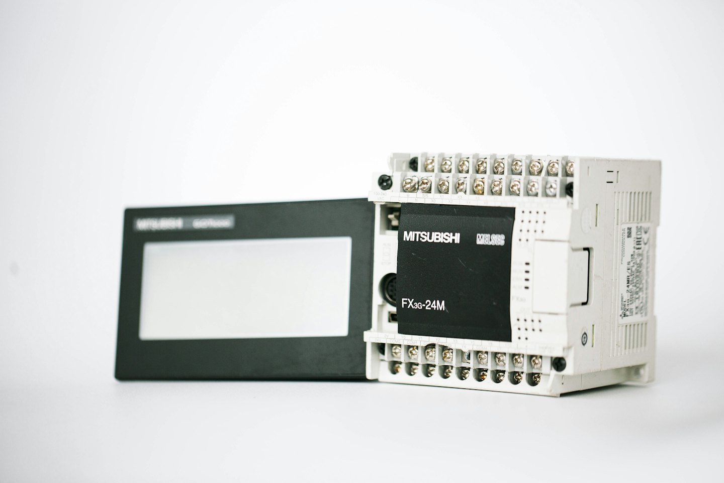 Pantalla de PLC e HMI industrial dispuesta sobre una superficie blanca.